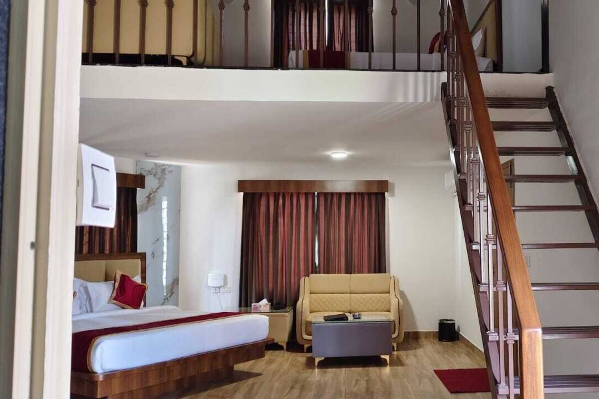 A hotel room with a bed, a sofa, a small table, a staircase, and a window with curtains.