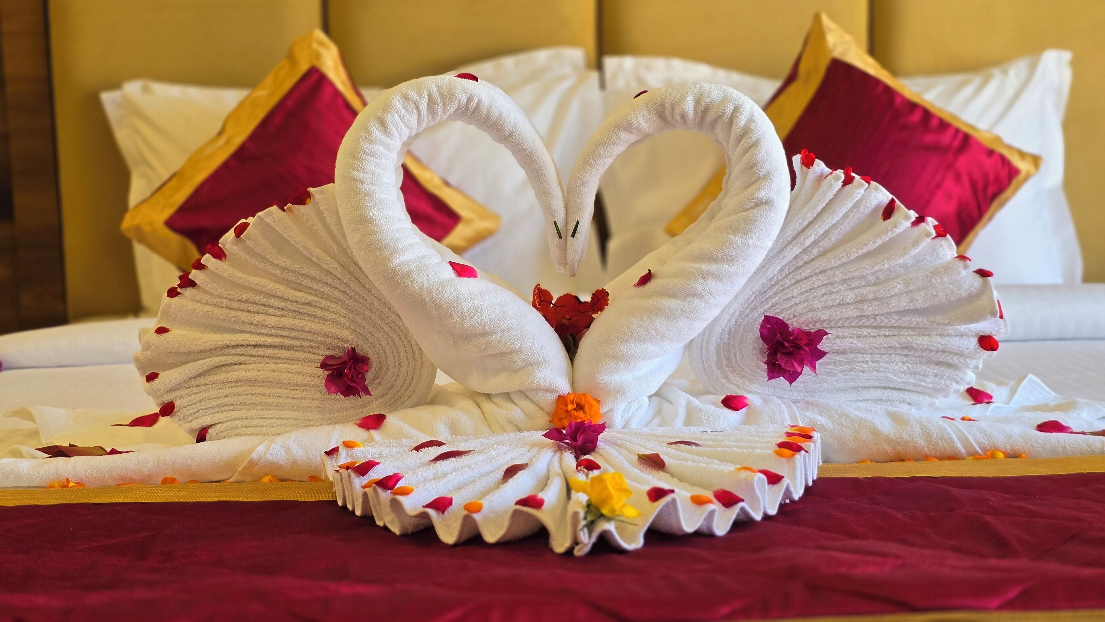 Een bed met decoratieve handdoeken in de vorm van zwanen, op een rode sprei.