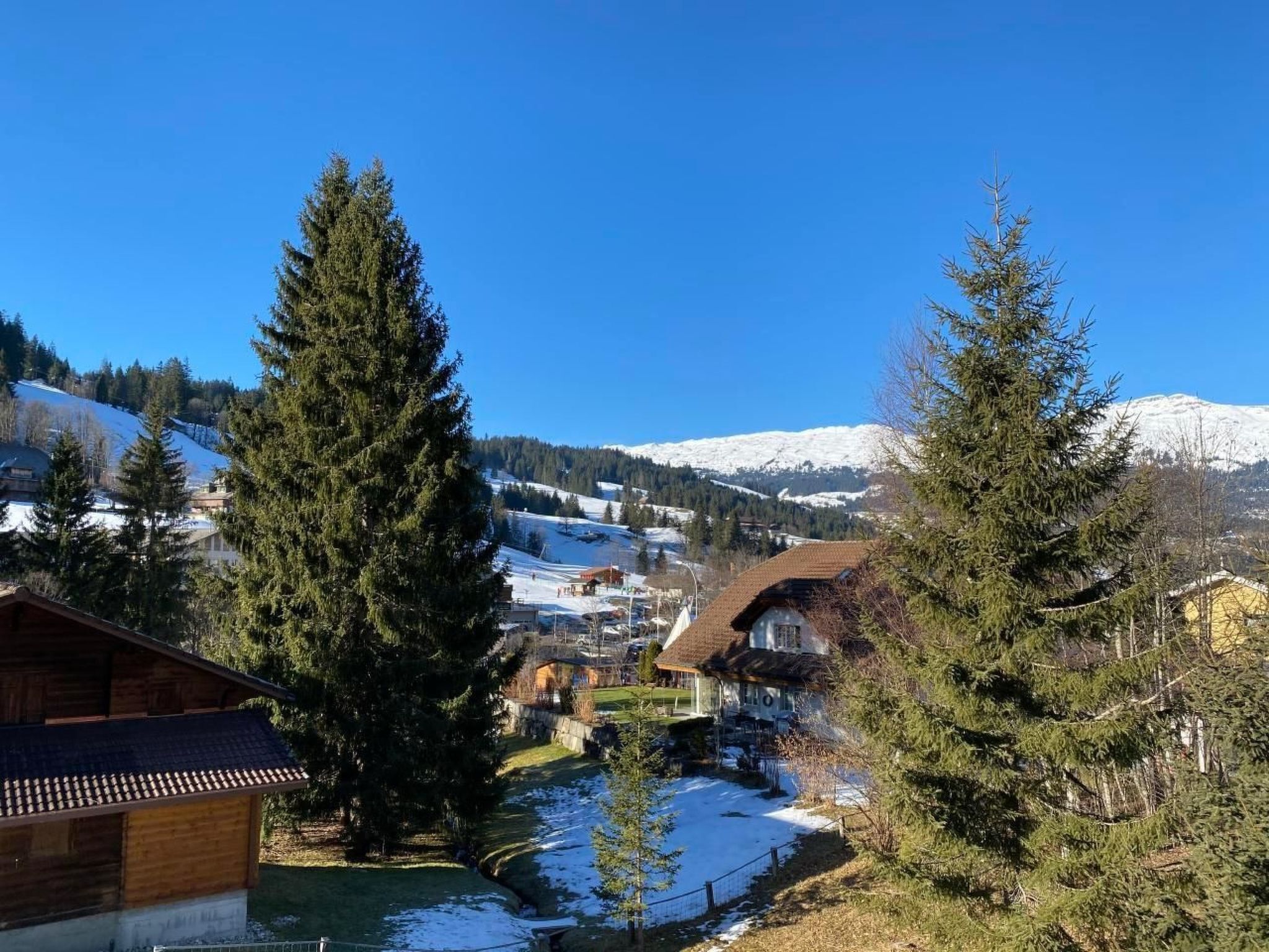 A mountainous village with snow-covered peaks, houses with sloped roofs, and a river running through the foreground.
