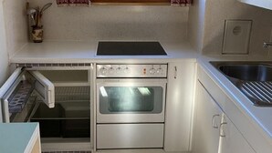 Uma cozinha compacta com forno embutido, pia e janela com cortinas estampadas.