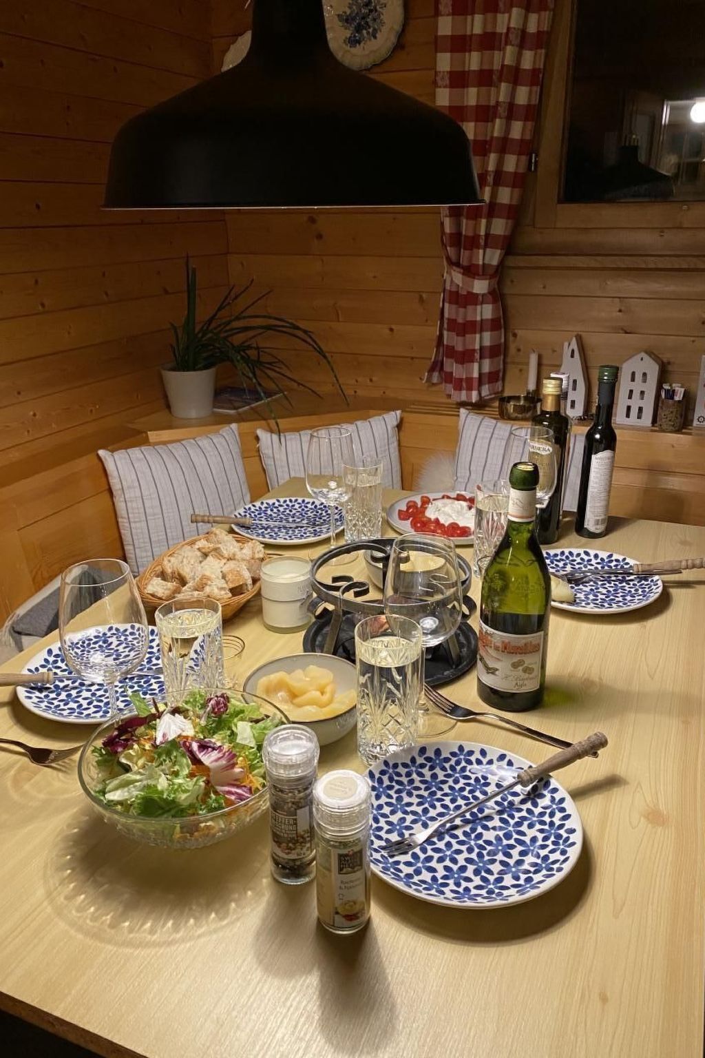 Una mesa de madera dispuesta con platos, vasos, una botella de vino y condimentos.