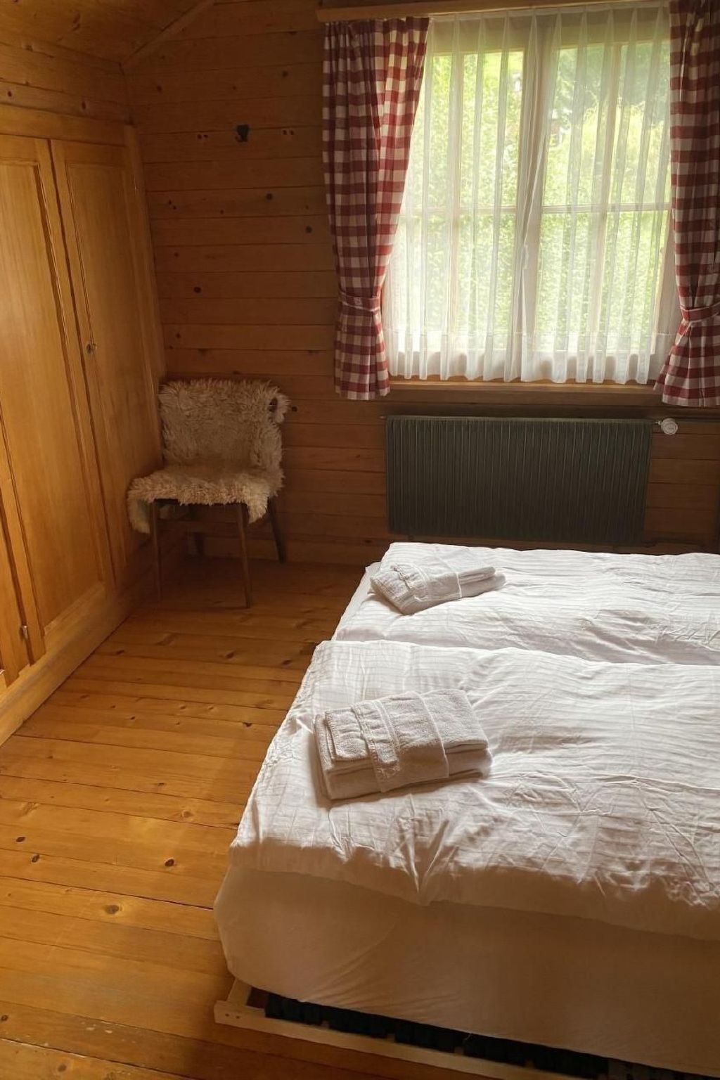 A wooden cabin room with a bed, a chair, and a window with curtains.