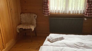 Quarto de cabana de madeira com cama, uma cadeira e janela com cortinas.