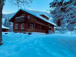 A wooden chalet with a balcony, surrounded by snow-covered trees and a mountainous backdrop. - Chalet Bacchus (OG) by Interhome (Sörenberg)
