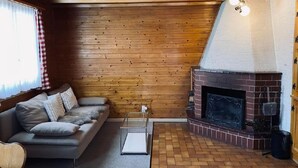 A cozy living room with a wooden ceiling, a fireplace, a sofa, and a window with curtains. - Chalet Bacchus (EG) by Interhome (Sörenberg)