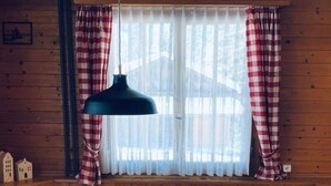 A wooden cabin interior with a dining table, two chairs, a red knitted placemat, and plaid curtains. - Chalet Bacchus (EG) by Interhome (Sörenberg)