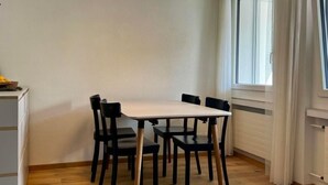 A dining area with a white table and black chairs, a pendant light, and a window with curtains.