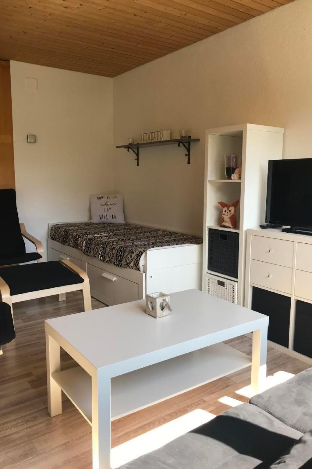 A modern, compact living space with a bed, a white table, a sofa, a TV, and a bookshelf.
