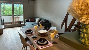 Ein Essbereich mit einem Holztisch, gedeckt für vier Personen, einer Couch und einem großen Fenster mit Blick ins Grüne.