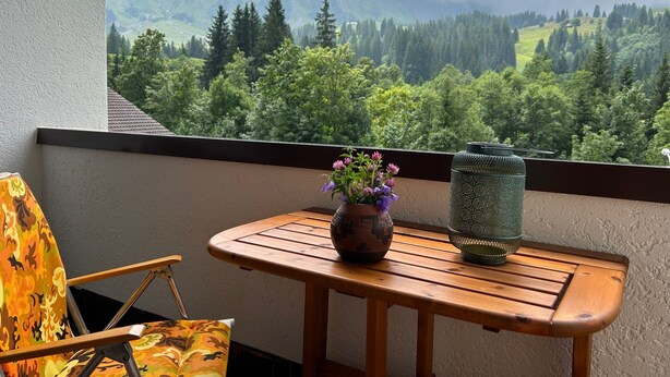 Ein Balkon mit Holztisch, einem Stuhl, einer Blumenvase und einer Laterne.