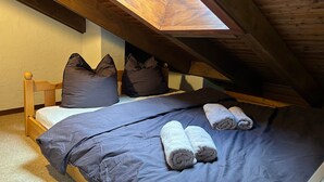 Ein Schlafzimmer mit schrägen Wänden, Holzbalken, einem Bett mit dunkler Bettwäsche und aufgerollten Handtüchern.