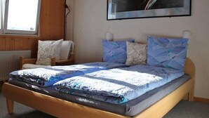 Un dormitorio con una cama de madera, una silla, un radiador y una ventana.