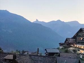 Eine Berglandschaft mit traditionellen Gebäuden, darunter ein markantes Haus mit geneigtem Dach und Schornstein.