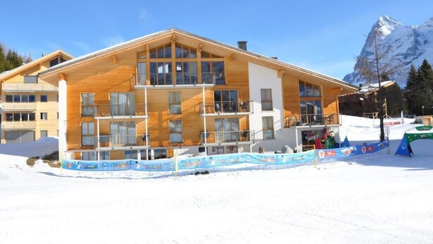 Un edificio de madera de varios pisos con balcones, con una imponente montaña nevada de fondo.