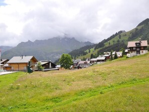 Ein ländliches Dorf mit traditionellen Holzhäusern, einem grasbewachsen Vordergrund und Bergen im Hintergrund.