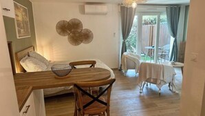Ein gemütliches Zimmer mit einem Bett, einem Esstisch mit Stühlen, einer Pendelleuchte und Blick ins Freie.