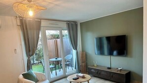 Ein Wohnzimmer mit einer Couch, einem Fernseher, einem kleinen Tisch und einer Glastür, die auf eine Terrasse führt.