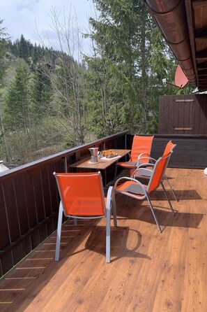 An outdoor deck with a wooden table and orange chairs, overlooking a forested area. - Chalet Bambi by Interhome (Sörenberg)