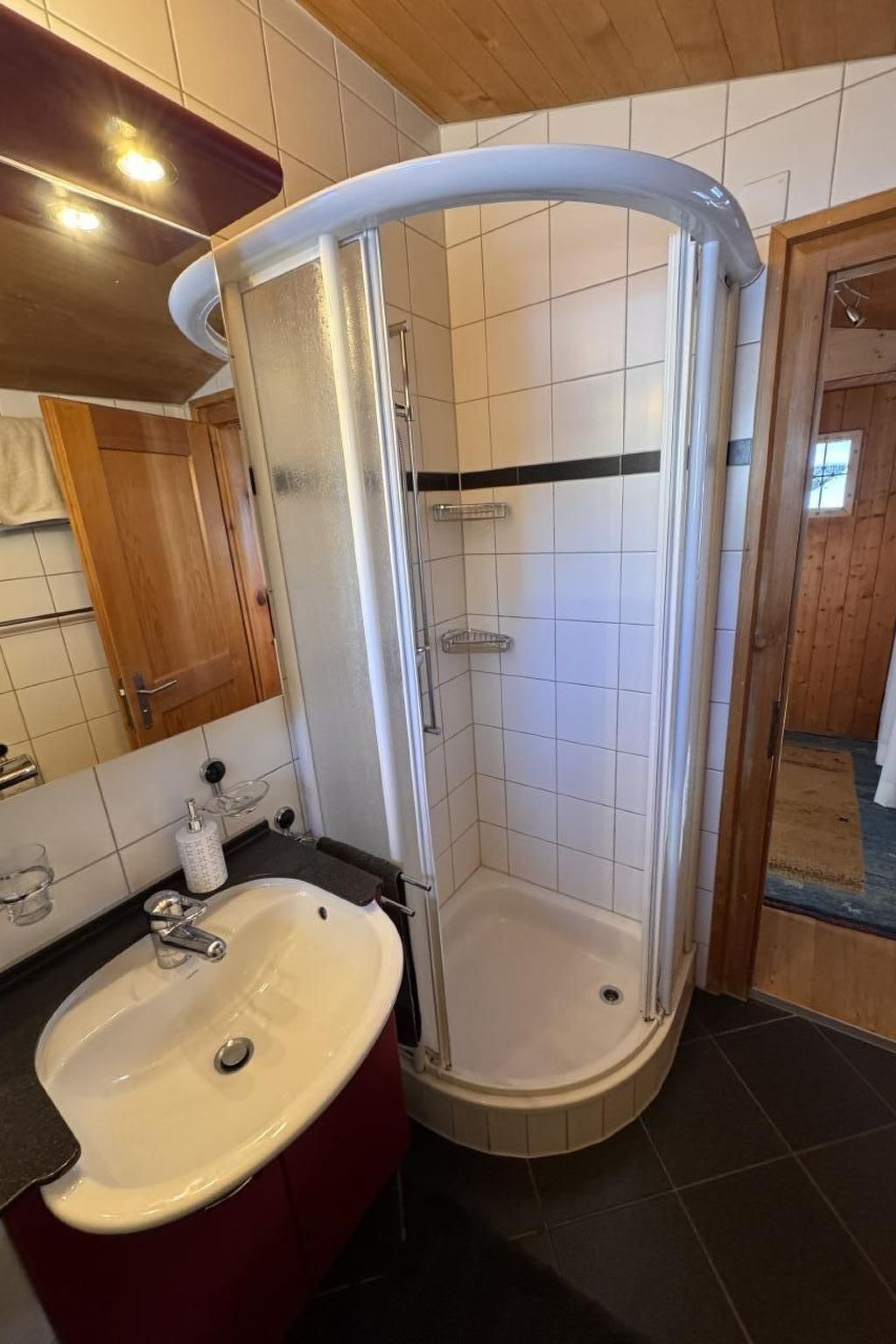 A bathroom with a white sink, a glass shower enclosure, and a wooden door.