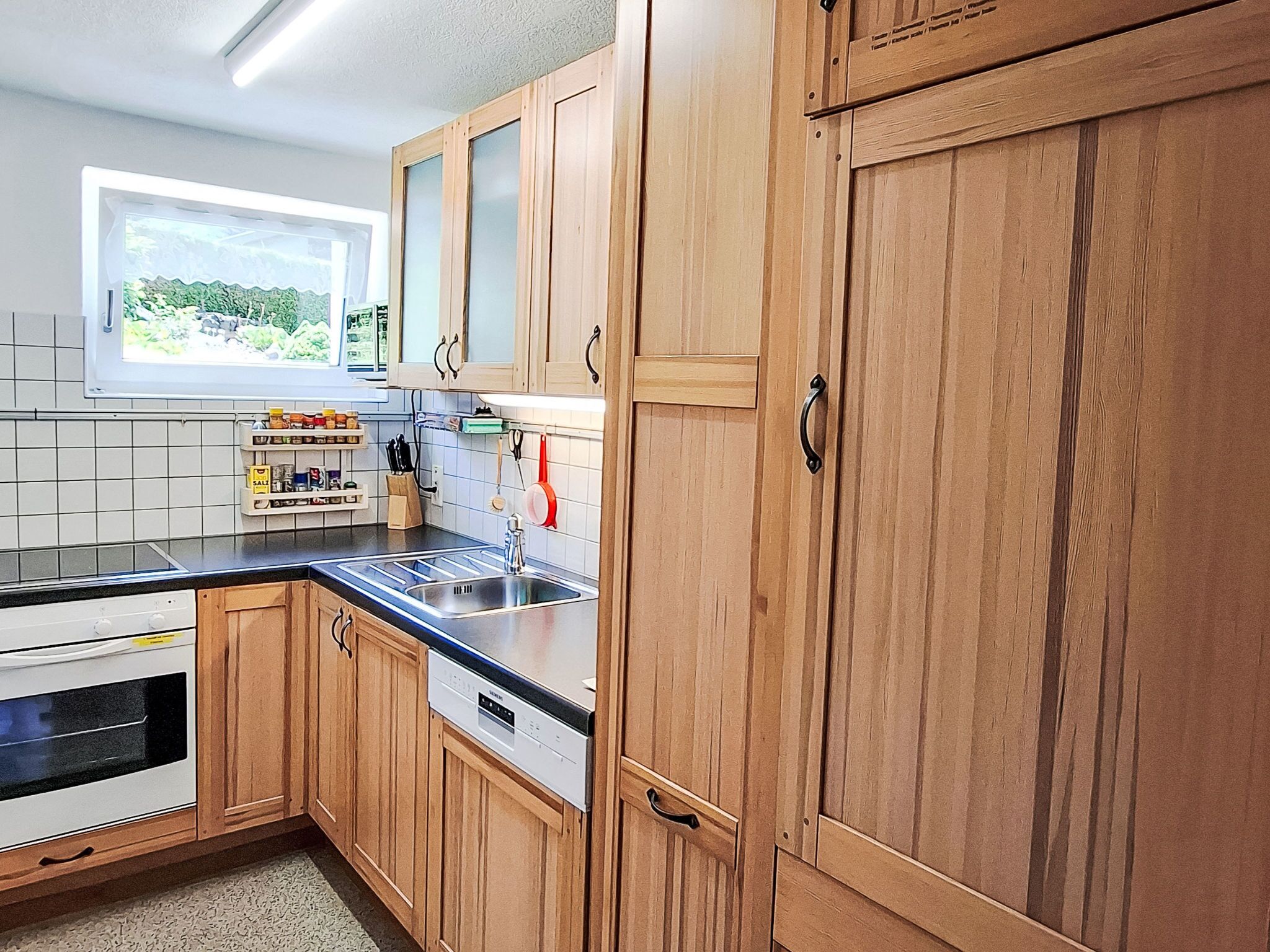 Cucina con mobili in legno, forno integrato, lavastoviglie e finestra vista su spazi verdi.