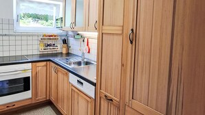 Ett kök med träskåp, en inbyggd ugn, en diskmaskin och ett fönster med utsikt över grönområden.
