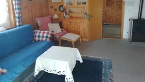 Tunnelmallinen huone, jossa on sininen sohva, pieni pöytä pitsiliinavaatteella, puinen kaappi ja tuoli, jossa on ruutukuvioinen koristetyyny.