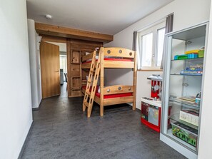 Una cama individual superpuesta con una escalera, un área de juegos con juguetes y un aparador de vidrio con juegos.