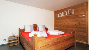 A wooden bed with a red mattress, pillows, and a nightstand with a lamp. - Schrattewohnung Birkenhof (4-Bett) by Interhome (Sörenberg)