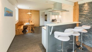 A modern kitchen with a central island, bar stools, and a stone accent wall. - Schrattewohnung Birkenhof (4-Bett) by Interhome (Sörenberg)