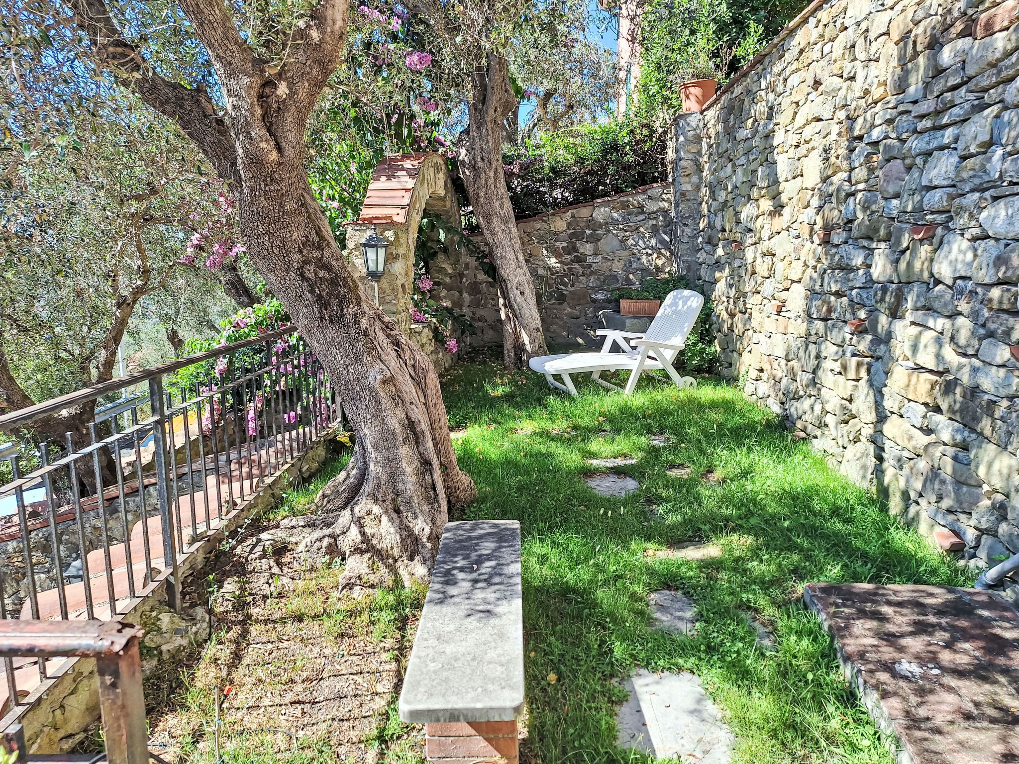 Un mur de pierre, une chaise blanche et un arbre aux fleurs roses.