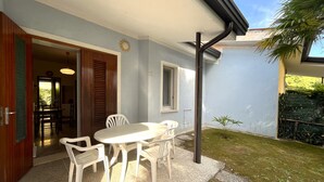 A patio with a table and chairs, a door leading to an interior space, and a small garden area. - VILLA CASTORINI - B2 4+0 - B3003C (Bibione Pineda)