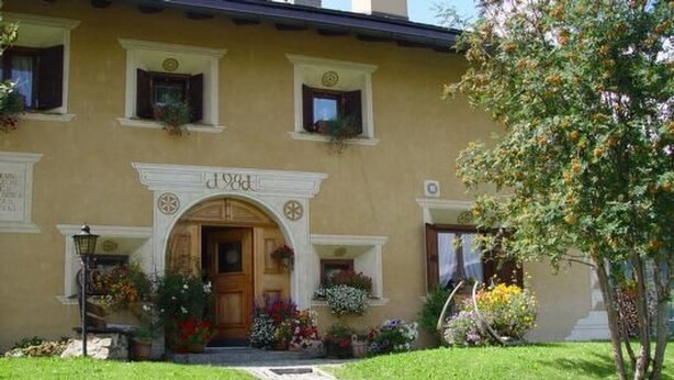 Un edificio con un ingresso centrale, un piccolo portico e un giardino con fiori e un albero.