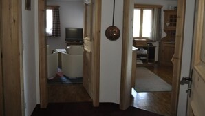 Un corridoio con porte in legno che conduce a una zona living con televisore, divano e una sala da pranzo con tavolo e sedie.