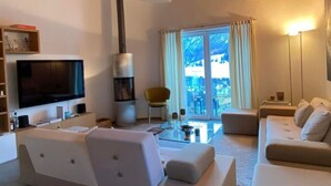 A modern living room with a large flat-screen TV, a fireplace, a sofa, and a dining area. - Chesa Baia by Interhome (La Punt-Chamues-ch)