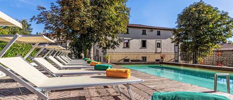 A poolside area with sun loungers, a pool, and a building in the background.