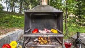 En udendørs grill med kød, grøntsager og brød, samt en flaske vin på et bord.