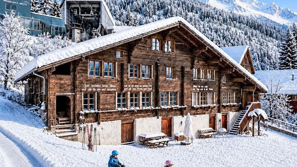 Un bâtiment en bois doté de nombreuses fenêtres et d’un toit en pente, entouré d’arbres et de montagnes couverts de neige.