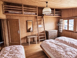 Una habitación de madera con literas, una escalera, un aparador y un ventanal con vistas.