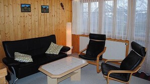 Puupaneloitu huone, jossa on musta sohva, kaksi mustaa nojatuolia ja laatoitettu sohvapöytä.