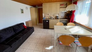 Un espacio habitable compacto con kitchenette, una zona de comedor con mesa y sillas, y un sofá negro.