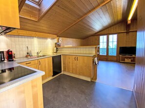Eine Küche mit Holzausstattung, Geschirrspüler, Kaffeemaschine und Fernseher in einem Loftraum mit schrägem Dach.