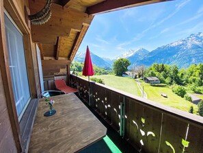 A wooden balcony with a table and chairs, a red umbrella, and a view of green fields and mountains. - FeWo Zenger-Jossi by Interhome (Hasliberg)