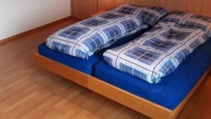 A room with a wooden ceiling, a bed with blue bedding, and a wall-mounted light fixture. - Schaad 8-Bettwohnung by Interhome (Hasliberg)