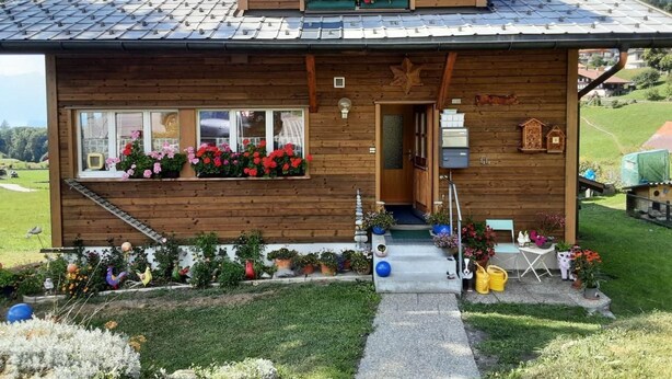 A wooden chalet with a sloped roof, large windows, flower boxes, and a small porch area.