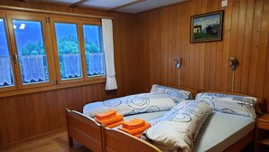 A wooden-paneled room with a bed, a window with curtains, and a painting on the wall.