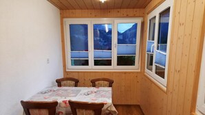 A small dining area with a table and four chairs, wooden walls, and large windows with a mountain view.