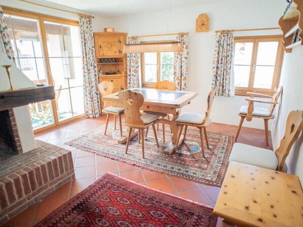 Comedor con una mesa y sillas de madera, chimenea y vistas a través de grandes ventanales.