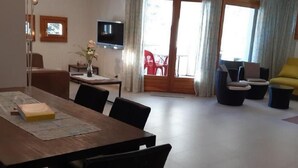 Ett modernt vardagsrum med ett matbord i trä, svarta stolar, en platt-TV och en soffa.