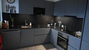 A modern kitchen with grey cabinetry, a black countertop, a microwave, an oven, and a sink. There is a clock on the wall and a plant on the counter. - Casa Leula by Interhome (Ronco sopra Ascona)