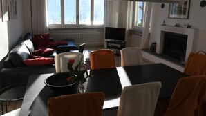 A living room with a sofa, a dining table, chairs, a TV, and a fireplace. - Casa Leula by Interhome (Ronco sopra Ascona)